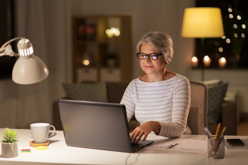 Older woman in glasses working on her laptop in a softly lit home office (Photo by Syda Productions - stock.adobe.com)